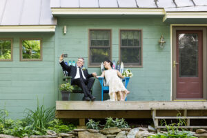 Newlyweds sit on a front porch in Vermont in Adirondack chairs made of skis and take a selfie