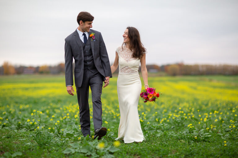 A wedding couple walks through a field dotted with little yellow flowers