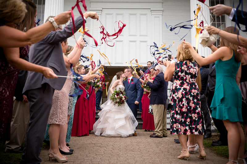 A newlywed couple is greeted with colorful ribbon wands held by their guests outside of the Stowe Community Church