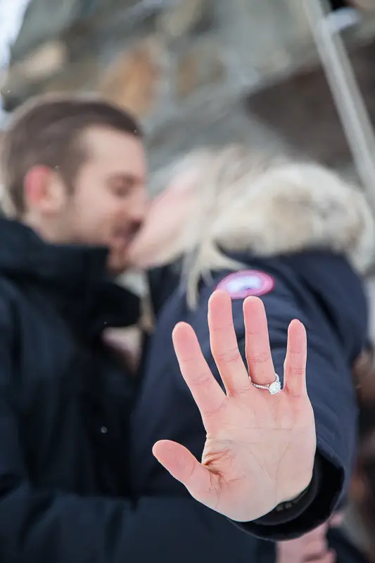 A newly engaged couple shows off the diamond engagement ring while they kiss at their Winter proposal at the Trapp Family Chapel in Stowe, Vermont