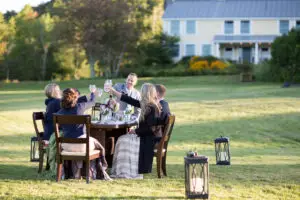 a dining table is set in a field with friends gathered for a wedding dinner
