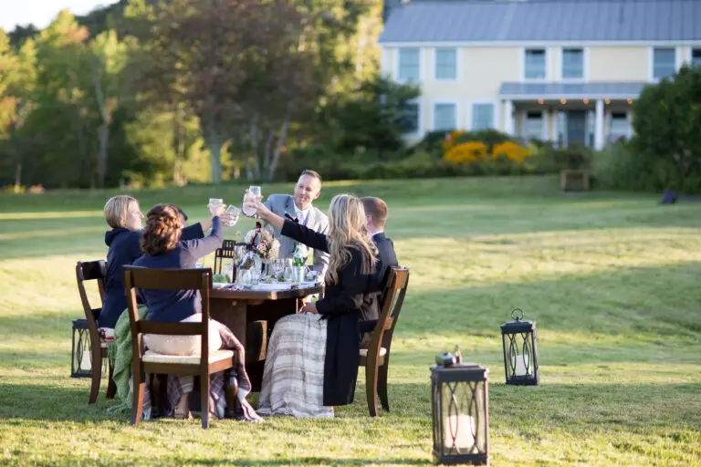 a dining table is set in a field with friends gathered for a wedding dinner