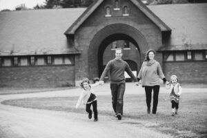 Family holds hands and runs across the field in front of the coach barn at Shelburne Farms, Vermont