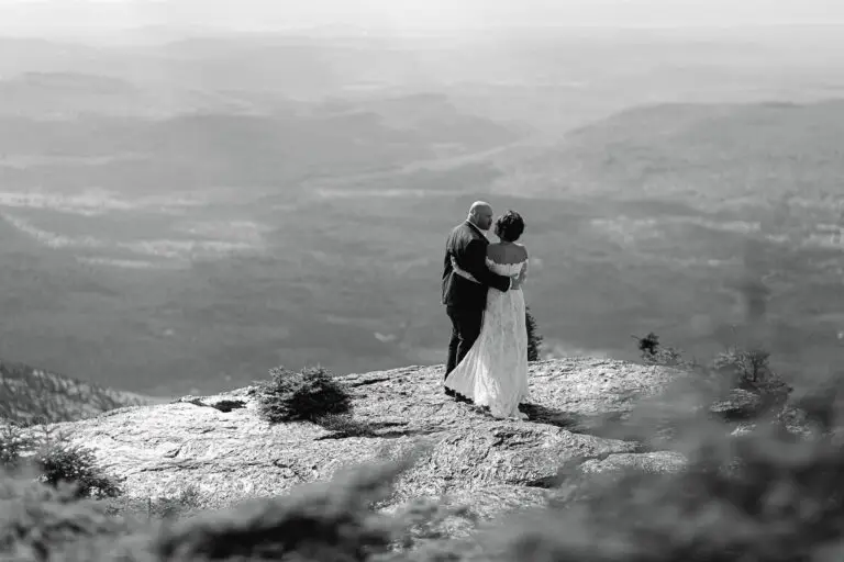 A bride and groom stand on the summit of mount mansfield, vermont