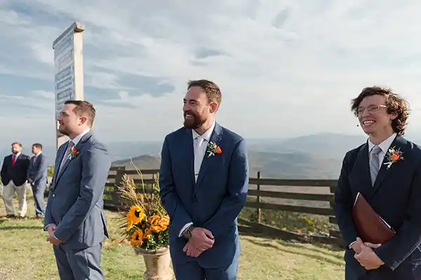 Groom peeks around wedding guests to catch first glimpse of bride walking down the aisle at Jay Peak summit ceremony.
