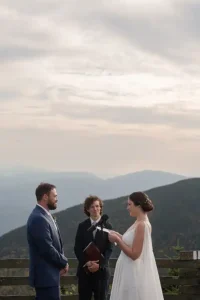 Couple exchanges vows at Jay Peak Resort summit ceremony as sunlight breaks through clouds during Vermont fall wedding.