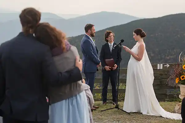 Couple exchanges vows at Jay Peak Resort summit ceremony as sunlight breaks through clouds during Vermont fall wedding.