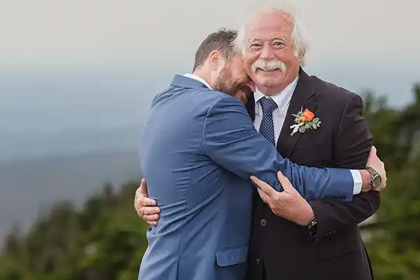 Groom gives characteristic warm full embrace to wedding guest during Jay Peak Resort Vermont fall wedding reception.
