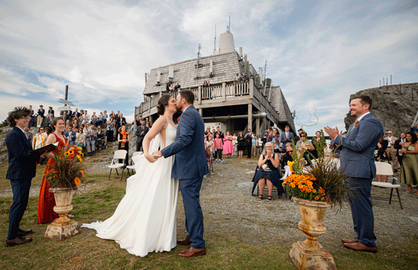 Couple shares first kiss as newlyweds at Jay Peak Resort summit outdoor wedding ceremony in Vermont fall.