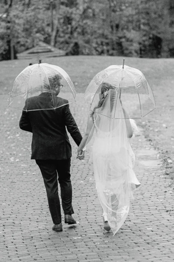 A wedding couple walks under umbrellas in the rain