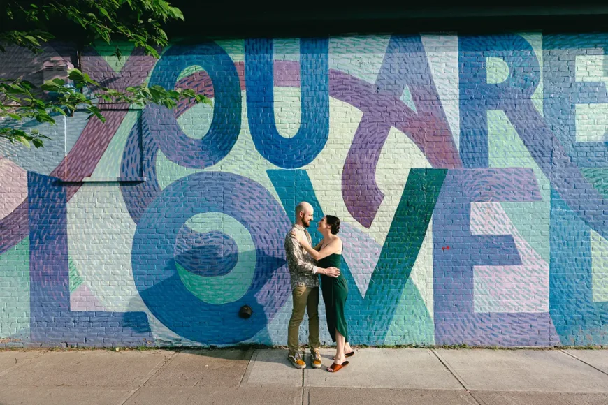 A couple stands in front of Burlingtons You are Loved mural on Cherry Street